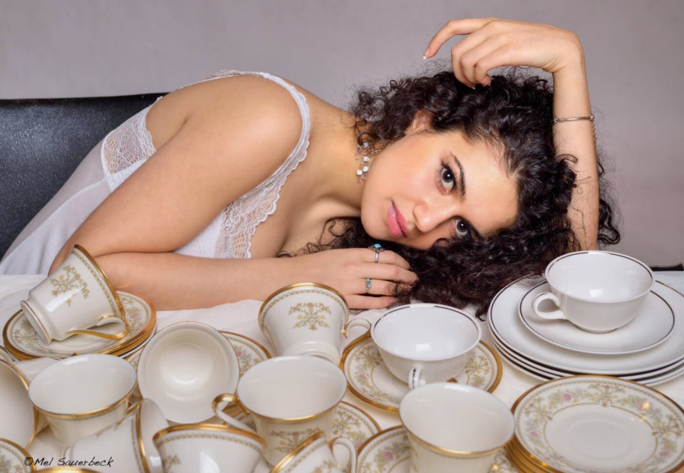 Beautiful dark, curly haired, young woman sitting with many tea cups